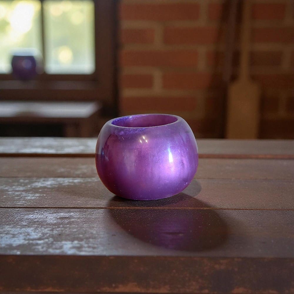 Round, purple pot on a wooden slatted bench. In the background is a brick wall and a window. There's a broom leaning up against the wall.