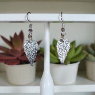 Silver leaf drop earrings hanging from a pole in front of green and red plants