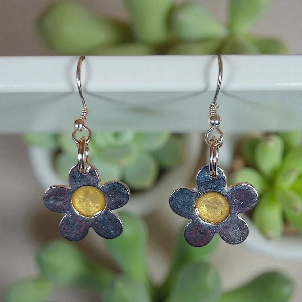 Silver daisy shaped earrings hanging from a pole in front of small plants