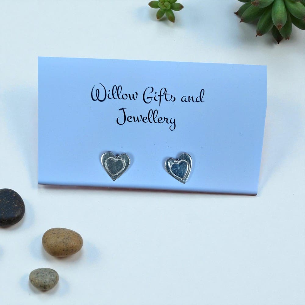 Silver heart shaped stud earrings on a white counter with small pebbles in front of them