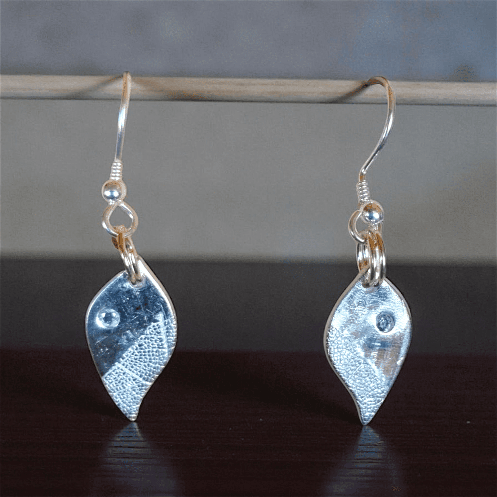 Silver leaf shaped earrings hanging from a pole. With skeleton leaf detail and set with cubic zirconia
