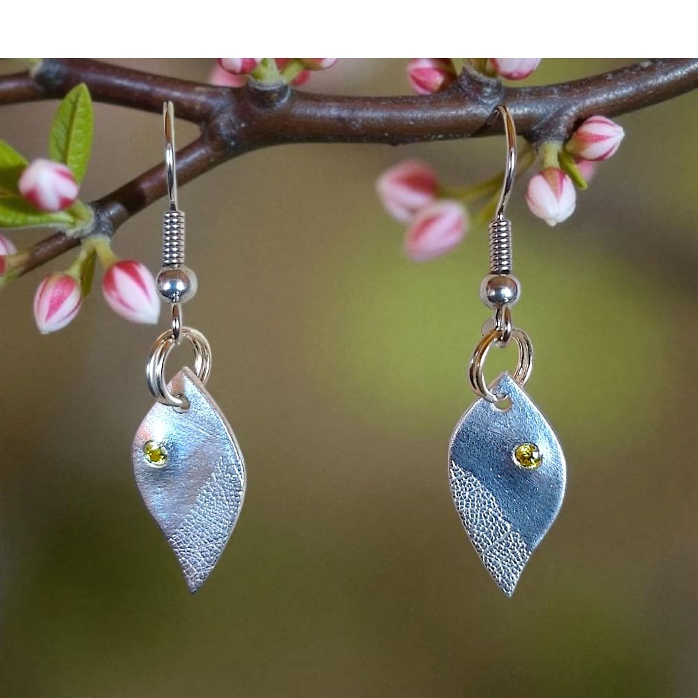 Silver leaf shaped drop earrings, with skeleton leaf detail, set with cubic zirconia hanging from a blossom branch