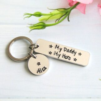slim rectangular aluminium keyring with the eords 'our daddy, our hero' hand-stamped on it with personalised name tags attached