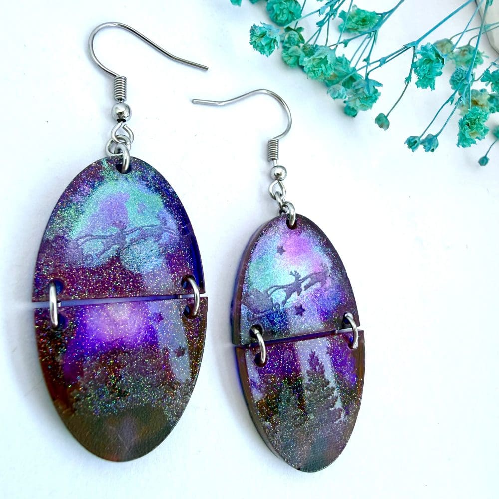 Purple and green aurora-style resin earrings showing Santa flying above trees, handmade split oval design