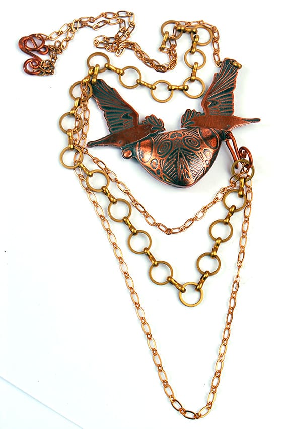 copper rook locket featuring two flying crows in a symmetrical design. Photographed on a white background showing the piece in it's entirety.