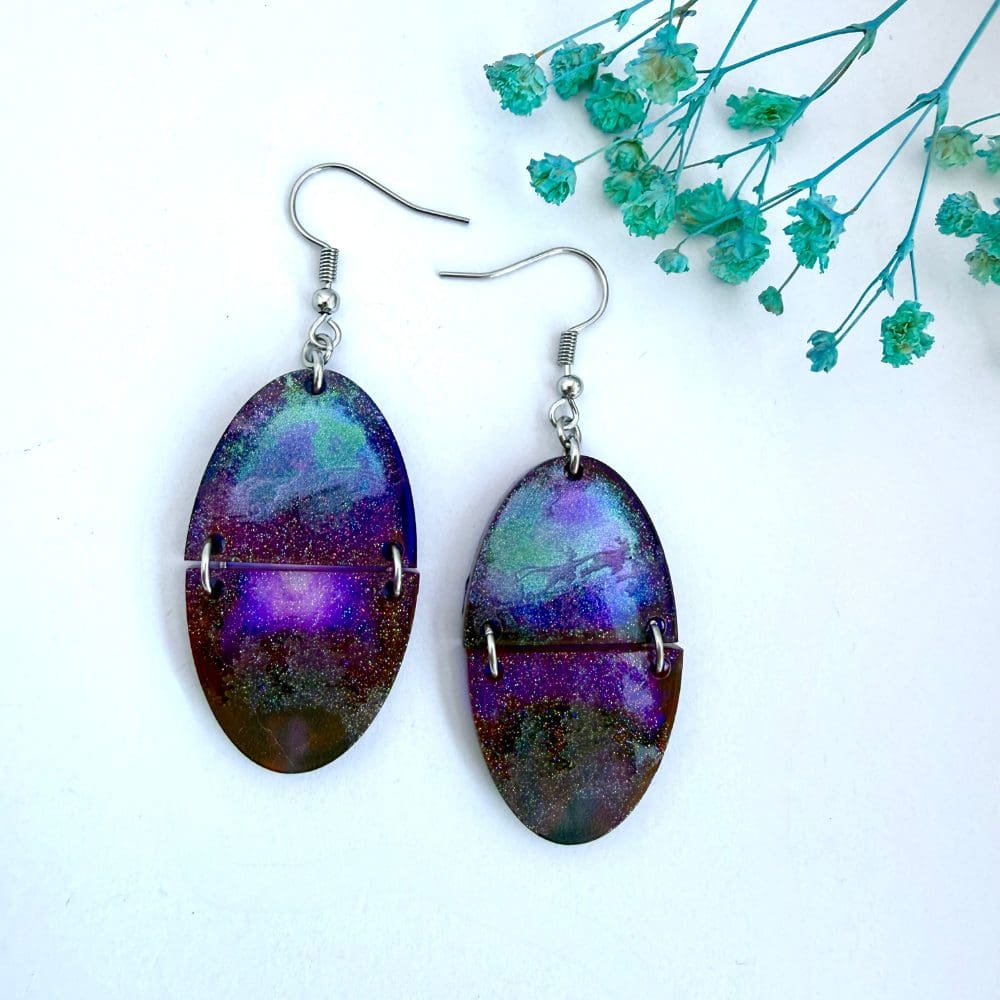 Handmade resin earrings with Santa and his sleigh etched over a purple and teal northern lights background, split oval design with glitter shimmer