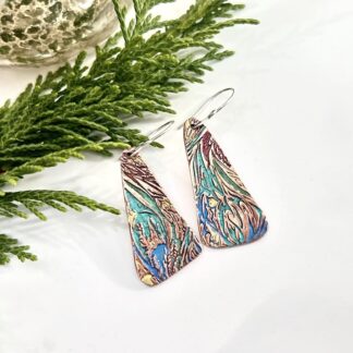 A pair of copper handcrafted drop earrings, long and textured in a swirl pattern and painted in blue, green and plum metallic colours. They have sterling silver ear wires and displayed on a white background.