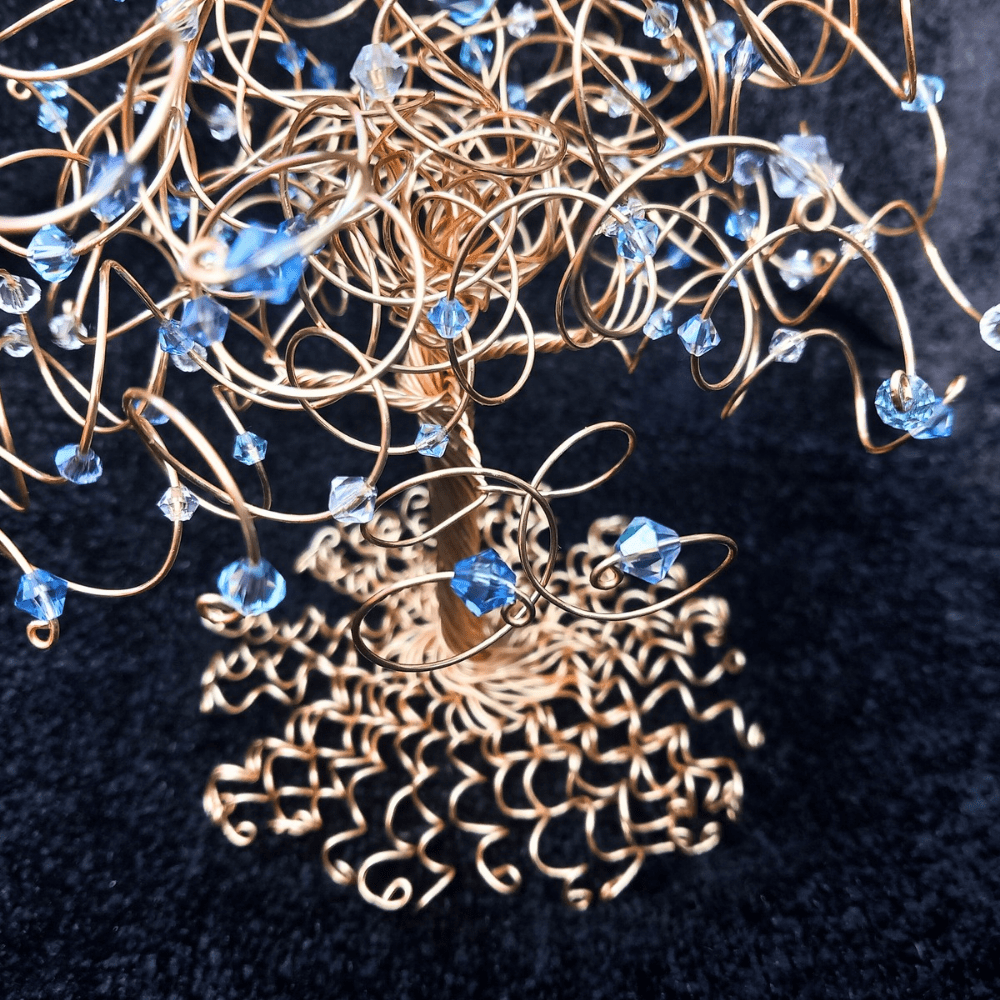Gold wire tree roots of the cake topper tree photographed with two entwined branches above them with a sapphire and aquamarine birthstone crystal on each.