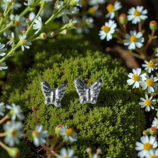 A pair of silver butterfly shaped earrings sitting on a bed of moss surrounded by white daisies