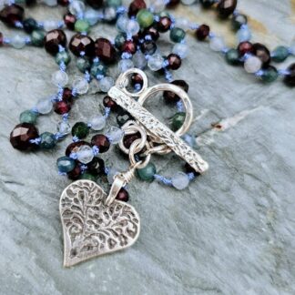 Aquamarine, blue tourmaline and red garnet gemstone necklace with silver folk heart, grey background heart detail, Isobel Kelly Jewellery
