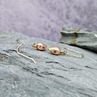 9ct gold drop earrings inspired by Roman amphora vessels, set with lab-grown diamonds and a central pink ruby, featuring twisted gold hooks. Side profile, on grey rock. Isobel Kelly Jewellery, Hants UK