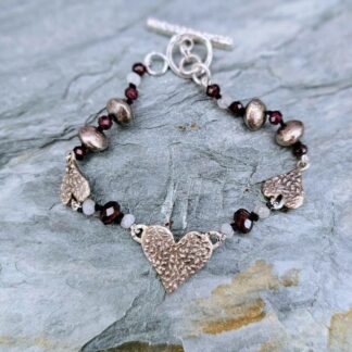 Handcrafted silver heart bracelet with antiqued etched charms, red garnet and moonstone beads on knotted silk, finished with a toggle clasp, Isobel Kelly Jewellery, Hants UK