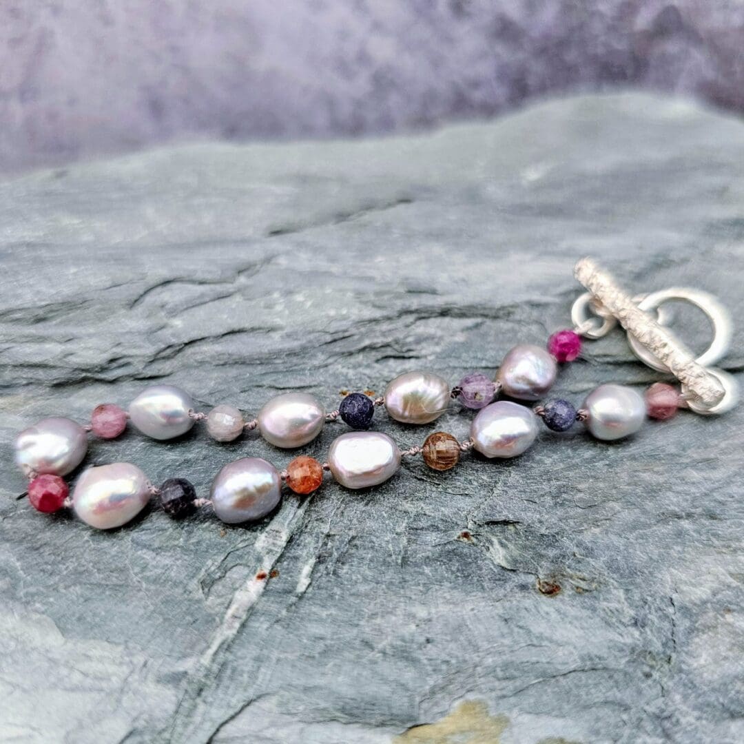 Baroque pearl, ruby and sapphire knotted bracelet, silver toggle, grey background, Isobel Kelly Jewellery