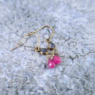 9ct gold earrings with rose-cut tanzanite bezels and dangling pink ruby briolettes, displayed on a textured stone surface. Isobel Kelly Jewellery, Hants UK