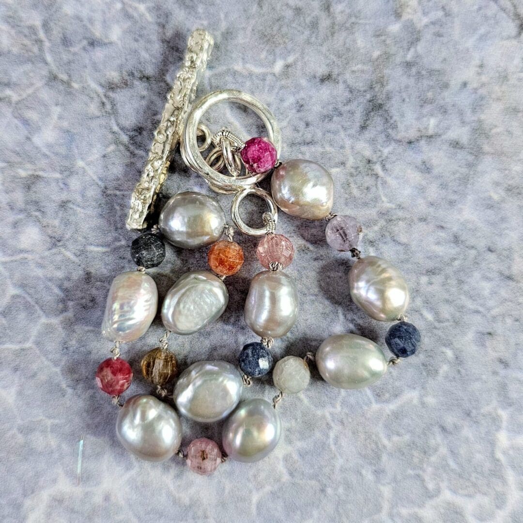 Baroque pearl, ruby and sapphire knotted bracelet, silver toggle, grey background bead closeup, Isobel Kelly Jewellery