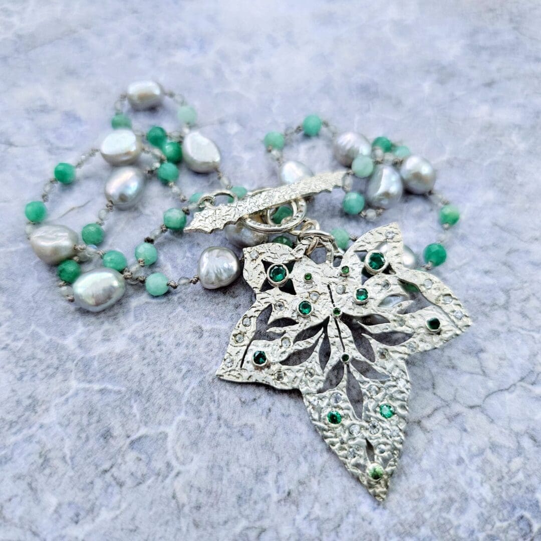 Etched sterling silver ivy pendant set with white sapphires, tsavorite garnets and lab emeralds, strung on a silk necklace with emerald, labradorite and baroque pearls. Pendant details. Isobel Kelly Jewellery, Hants UK