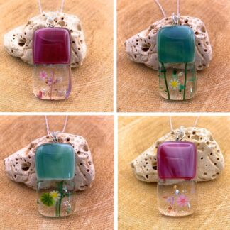 Colorful glass jewelry pendants with botanical designs, displayed on natural rock, arranged in a 2x2 grid.