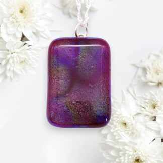 A vibrant purple rectangular pendant with iridescent tones hangs from a silver chain, surrounded by soft white chrysanthemums on a white background.