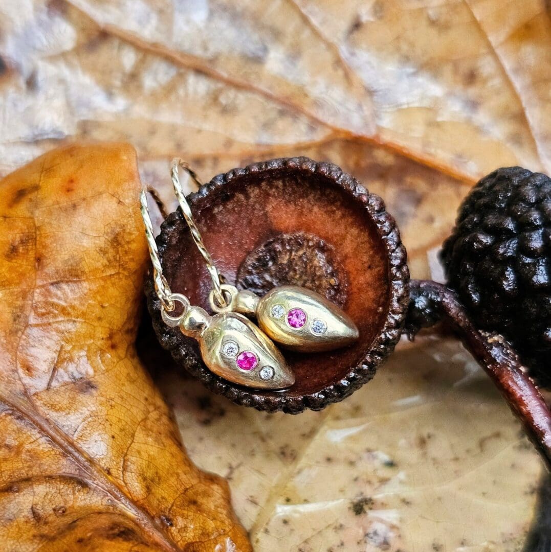 9ct gold drop earrings inspired by Roman amphora vessels, set with lab-grown diamonds and a central pink ruby, featuring twisted gold hooks. Outdoor shop, acorn cup. Isobel Kelly Jewellery, Hants UK