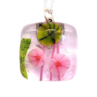 A colorful pendant featuring pink flowers and a green decorative element encased in resin, hung on a silver chain.