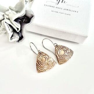A pair of handcrafted bronze triangular drop earrings that have a swirl textured raised pattern. They have sterling silver ear wires and are displayed on a white gift box