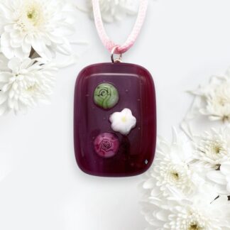 A maroon pendant featuring three floral designs in green, pink, and white, surrounded by white chrysanthemums.