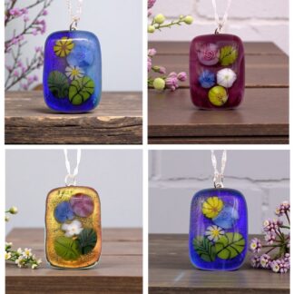 Four decorative glass pendants featuring vibrant floral designs in blue, purple, and gold hues, displayed on wooden surfaces.