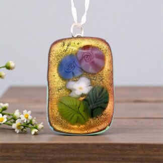 A colorful floral pendant featuring blue and purple roses, a white flower, and green leaves, set against a golden background.