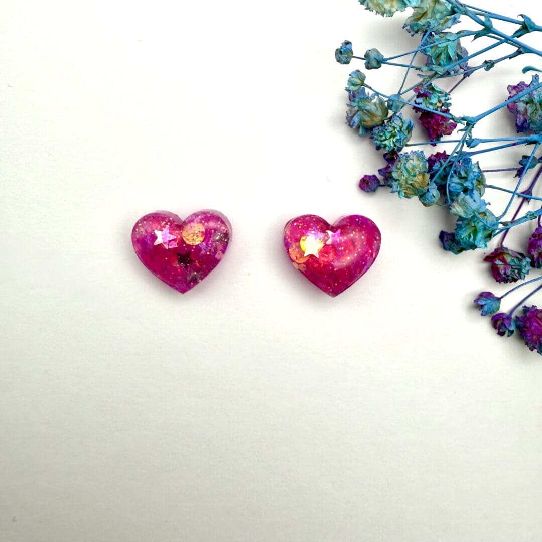 Pink glitter resin jewellery with romantic heart design. Displayed on a white background.