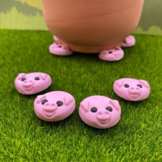 A terracotta pot rests on pink pig pot feet, with four more scattered on the artificial grass in front of it, which shows there smiling faces.