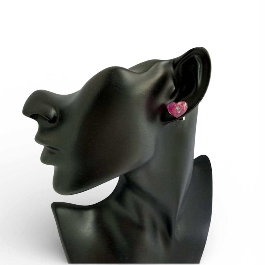 Pink glittery love heart stud earrings on a bust showing the size.