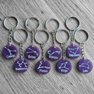 “Resin star sign keyrings with zodiac constellation designs on purple background”