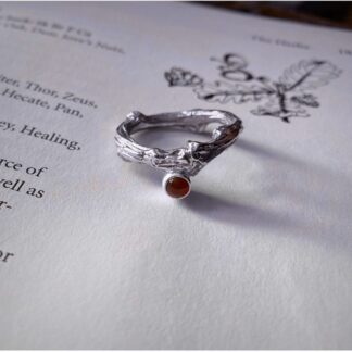 A ring cast from a small branch is o top of an open book facing slightly to the left. It is set with an orange- red carnelion cabochon in a full bezel setting.