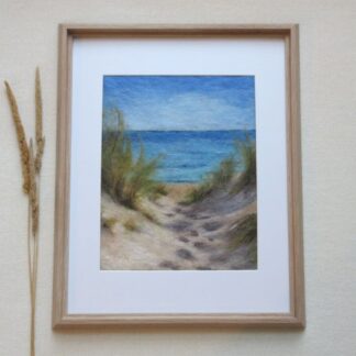 A view of blue sea and sky through sand dunes. There are tufts of grass growing from the top of the dunes and foot prints in the sand. Stems of grass are displayed by the side of the frame.