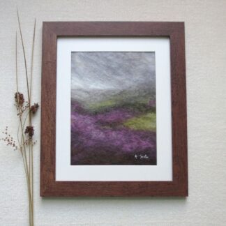 Wool felted dark grey rain clouds over a moorland with purple heather in bloom. Stems of rushes are displayed by the side of the frame.