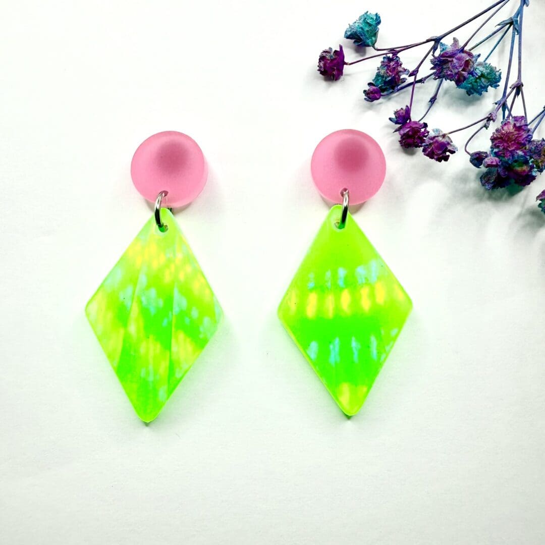 Glow in the dark neon green earrings with pink stud topper with a holographic finish. On surgical steel studs and backs displayed on a white background.