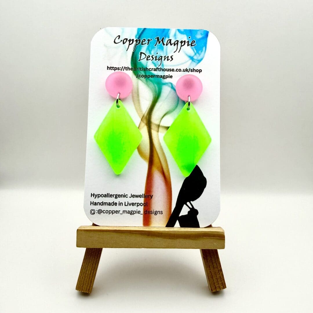 Neon green glow resin earrings with geometric diamond shape design displayed on a branded Copper Magpie Designs card.