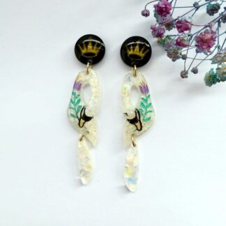 Handmade resin swan statement earrings with opalescent shimmer hanging from a black stud topper with gold crown.
