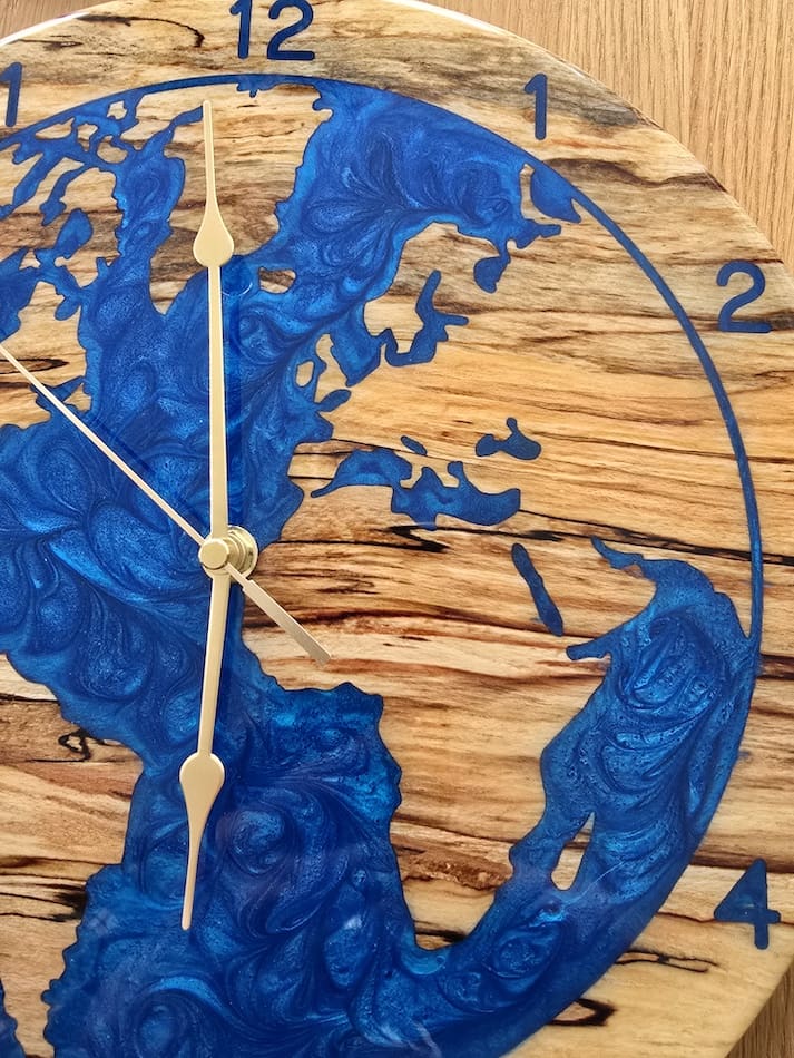 Spalted beech world map wall clock with deep blue resin oceans and integrated LED halo backlight, 315mm handmade wooden clock by The Humble Woodshed.