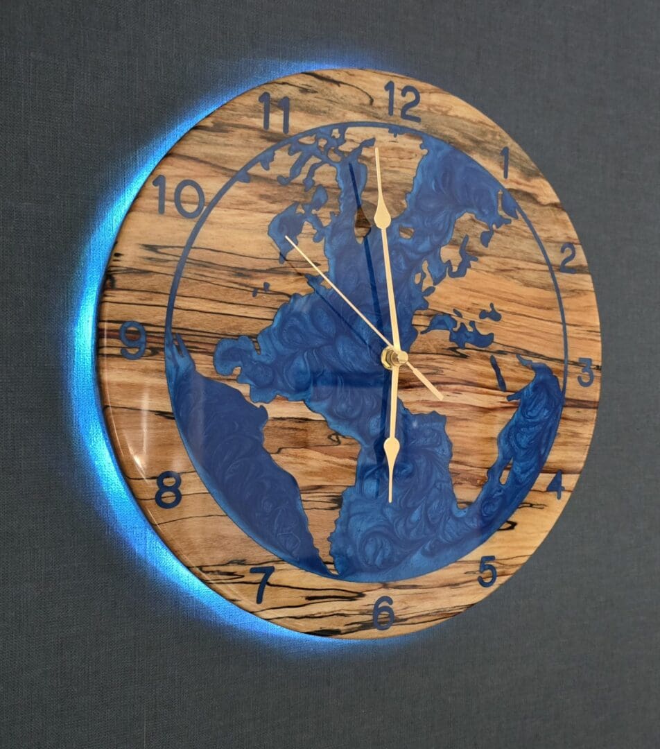 Spalted beech world map wall clock with deep blue resin oceans and integrated LED halo backlight, 315mm handmade wooden clock by The Humble Woodshed.