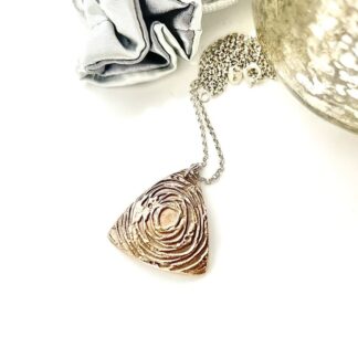 A handcrafted bronze triangle shaped pendant that has a swirl textured raised pattern. It has a sterling silver chain and is displayed on a white background.