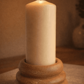 Handcrafted lacewood pillar candle holder with stacked sculptural base and lit ivory candle, photographed in warm ambient light.
