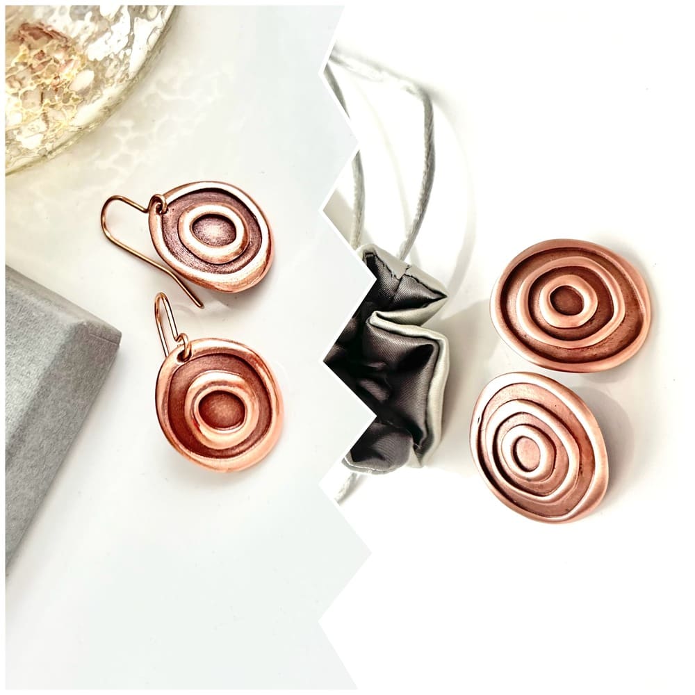 Two pairs of copper earrings, one large and stud the other small and drop, they have a raised circle texture. They are displayed side by side ans on a white background sitting next to each other.