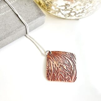A pair of handcrafted triangle shaped copper drop earrings with a large hole for the sterling silver ear wires.These textured earrings are displayed on a white textured background.