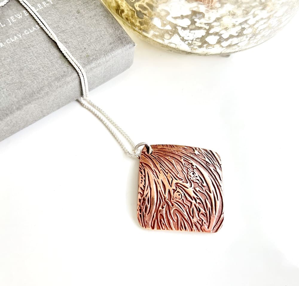 A pair of handcrafted triangle shaped copper drop earrings with a large hole for the sterling silver ear wires.These textured earrings are displayed on a white textured background.
