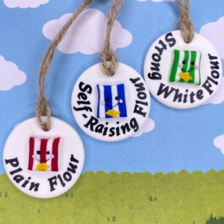 Three round kitchen labels with charming food-themed decorations. Each white label contains a striped bag with smiling face, in red, green and blue. Each one with the additional wording - Plain flour, Strong White Flour and Self Raising Flour.