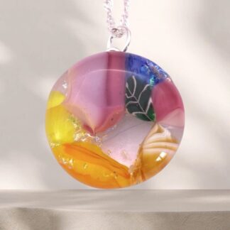 Colorful handmade glass pendant featuring pink, yellow, and blue swirls, detailed with a leaf design, suspended on a silver chain.
