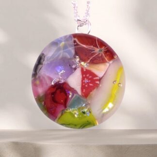 Colorful dichroic glass pendant featuring embedded flowers and vibrant patterns, hanging from a delicate chain against a soft background.