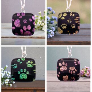 Four colorful paw print pendants on a black background, featuring glittery designs in pink, gold, and green, arranged artistically.