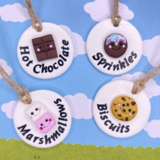 Four round kitchen labels with charming food-themed decorations: a chocolate bar for "Hot Chocolate", a cookie with sprinkles for "Sprinkles", stacked marshmallows for "Marshmallows", and a chocolate chip cookie for "Biscuits".